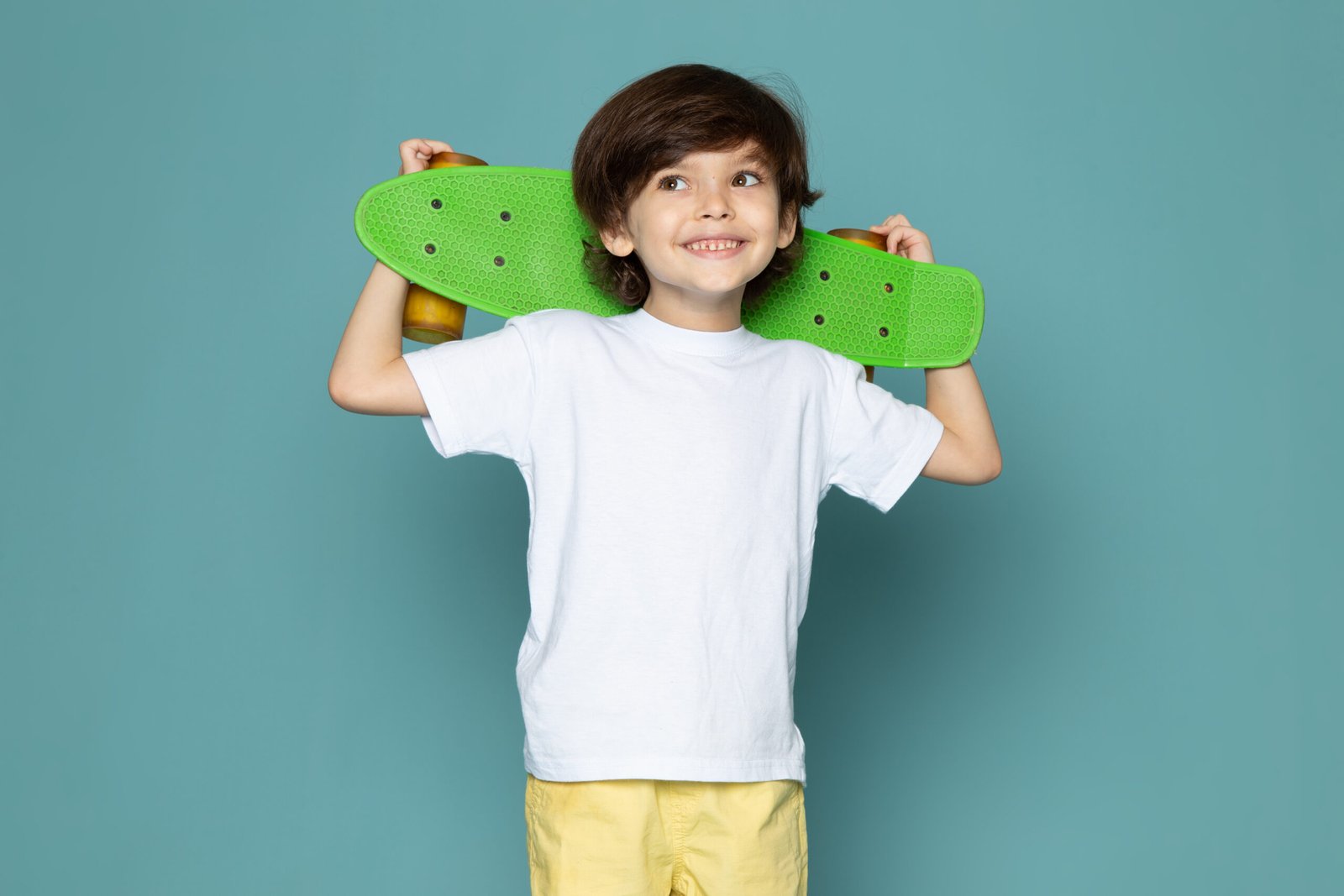 front-view-cute-boy-white-t-shirt-yellow-jeans-holding-green-skateboard-blue-space